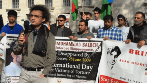 Baloch political activist Aomar Karim delivering a speech at the Baloch National Movement UK Chapter protest outside 10 Downing Street, London, on 8 April 2026, with activists holding banners demanding justice for enforced disappearance victims including Mohammad Baloch and Asad Baloch.