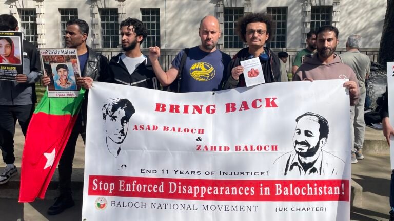 Baloch political activist Aomar Karim (right) and trade union activist Sacha Ismail (centre, raised fist) stand with fellow Baloch activists outside 10 Downing Street, London, holding a banner demanding the return of enforced disappearance victims Asad Baloch and Zahid Baloch, during the Baloch National Movement UK Chapter protest on 8 April 2026.